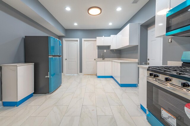 kitchen featuring freestanding refrigerator, stainless steel gas stove, light countertops, white cabinetry, and a sink