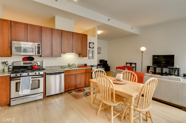 kitchen featuring brown cabinets, appliances with stainless steel finishes, a sink, light wood-style floors, and open floor plan