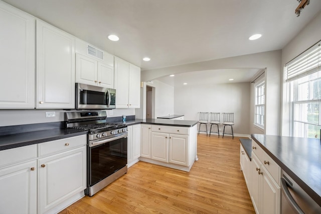 1578 Mccraren Rd, Highland Park, IL 60035 - kitchen featuring appliances with stainless steel finishes, dark countertops, arched walkways, light wood-style flooring, and recessed lighting