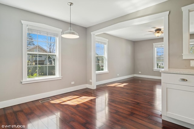 unfurnished dining area featuring a ceiling fan, baseboards, visible vents, and dark wood-style floors