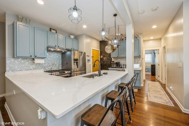 kitchen with blue cabinetry, a sink, a peninsula, under cabinet range hood, and stainless steel appliances