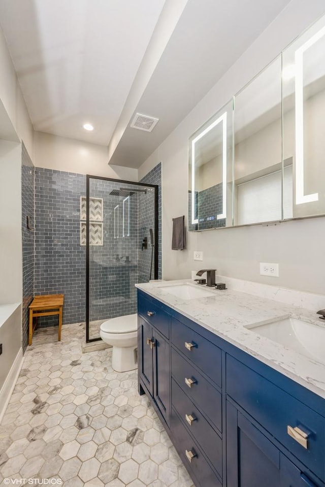 bathroom with toilet, tiled shower, a sink, and visible vents