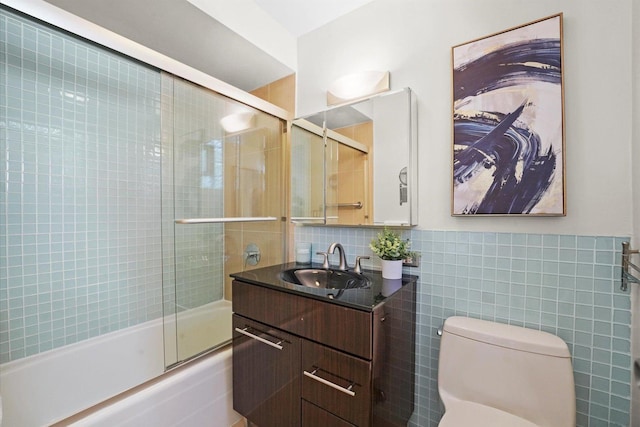 bathroom with toilet, tile walls, bath / shower combo with glass door, and vanity