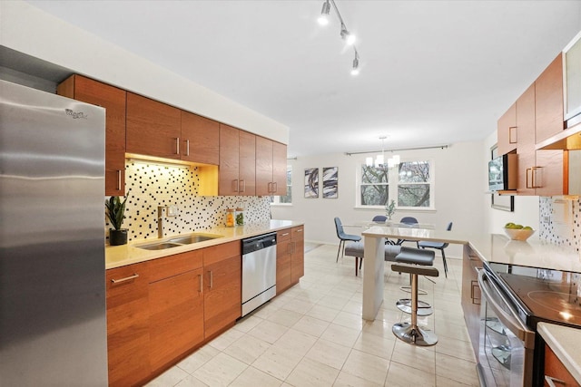 kitchen with backsplash, appliances with stainless steel finishes, a sink, light countertops, and a notable chandelier