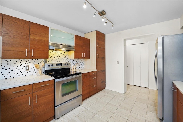 kitchen featuring appliances with stainless steel finishes, light countertops, tasteful backsplash, under cabinet range hood, and glass insert cabinets