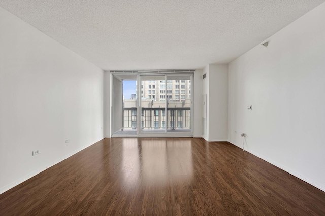empty room with a textured ceiling, dark wood-type flooring, baseboards, and a wall of windows