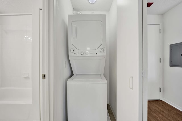 laundry area featuring stacked washer / dryer, electric panel, baseboards, and dark wood-type flooring