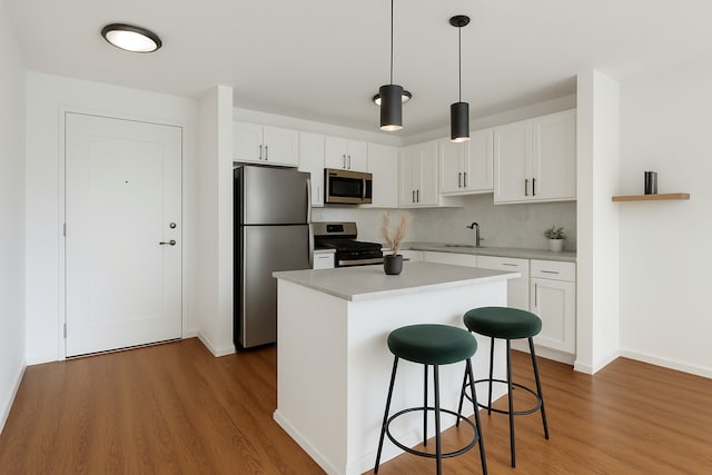 kitchen with appliances with stainless steel finishes, a sink, wood finished floors, and white cabinets