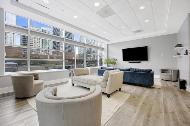 living area featuring baseboards, light wood-type flooring, a drop ceiling, and recessed lighting