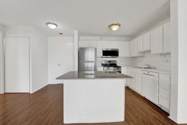 kitchen featuring appliances with stainless steel finishes, white cabinets, dark wood finished floors, a sink, and a kitchen island
