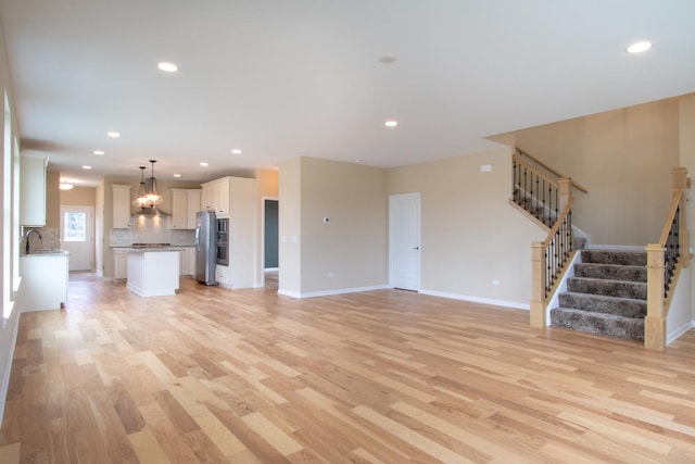 unfurnished living room featuring recessed lighting, light wood finished floors, and stairs