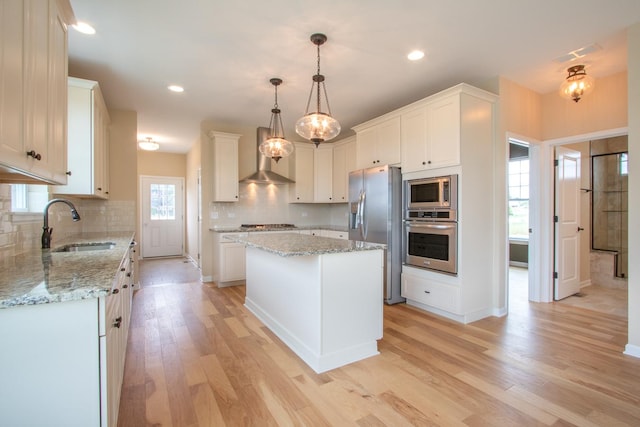 kitchen featuring a kitchen island, tasteful backsplash, a sink, light wood finished floors, and stainless steel appliances