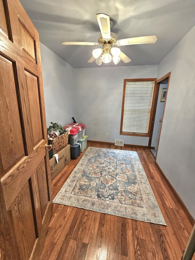 interior space with visible vents, a ceiling fan, dark wood finished floors, and baseboards