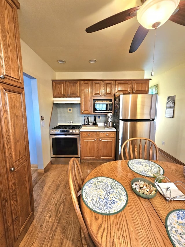 kitchen with backsplash, wood finished floors, light countertops, under cabinet range hood, and stainless steel appliances