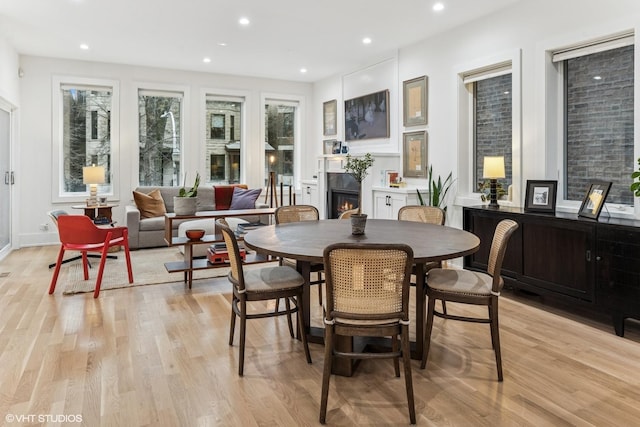 dining area with recessed lighting, a lit fireplace, and light wood-style flooring