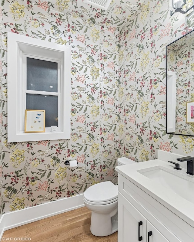 bathroom with vanity, toilet, wallpapered walls, wood finished floors, and visible vents