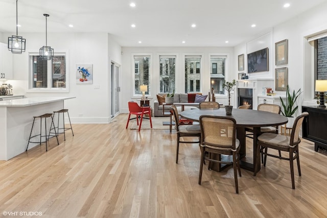 dining room with recessed lighting, baseboards, light wood-type flooring, and a warm lit fireplace