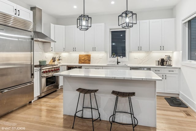 kitchen with wall chimney range hood, a sink, a kitchen breakfast bar, recessed lighting, and premium appliances