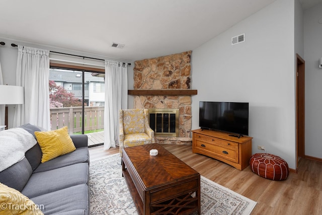 living area featuring a stone fireplace, visible vents, baseboards, lofted ceiling, and light wood-style flooring