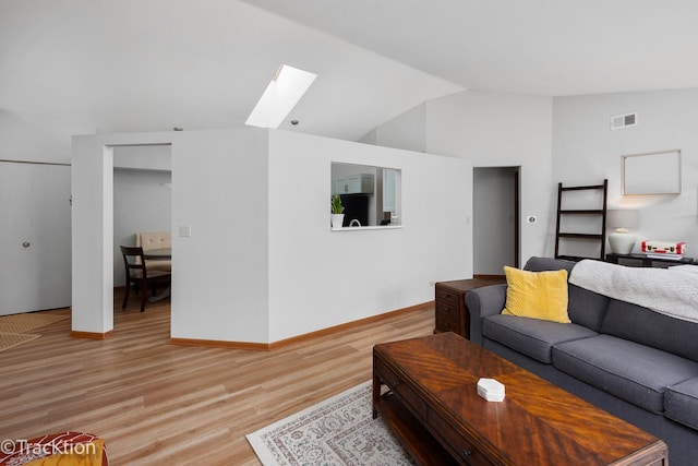 living room featuring baseboards, visible vents, vaulted ceiling with skylight, and light wood-style floors