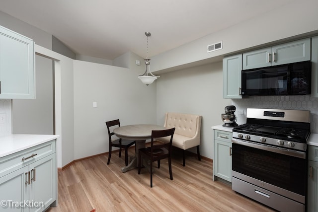 kitchen featuring stainless steel gas range, black microwave, light countertops, decorative backsplash, and visible vents