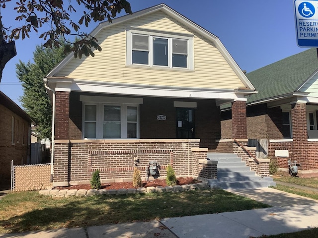 view of front of house featuring a porch, a gambrel roof, fence, and brick siding