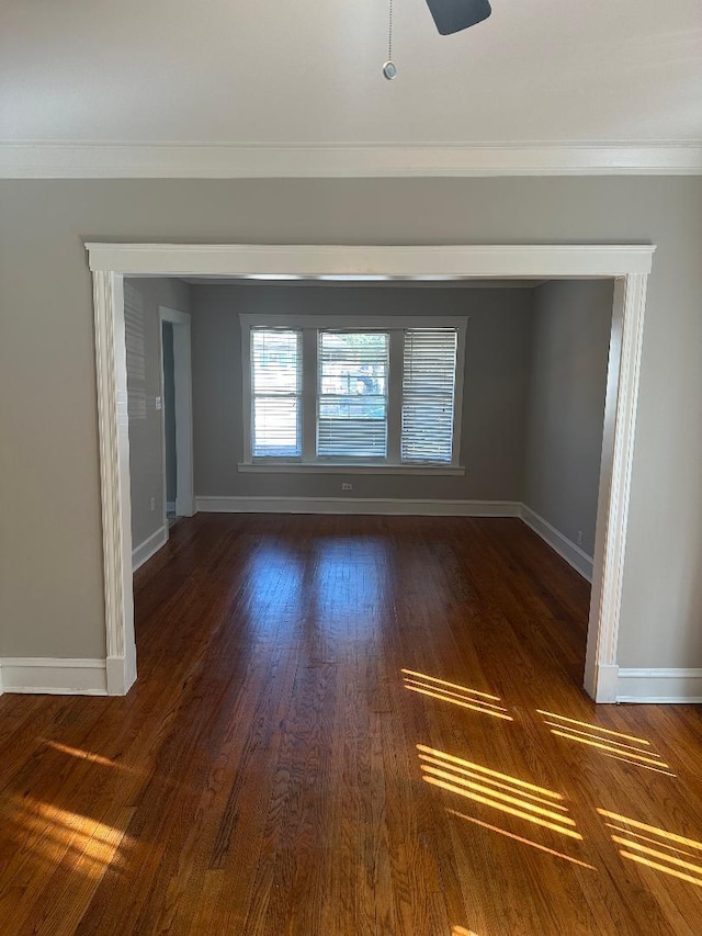 unfurnished room featuring a ceiling fan, baseboards, dark wood finished floors, and ornamental molding