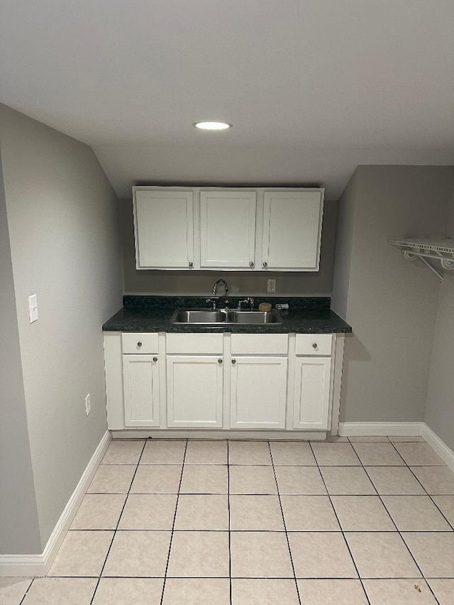 kitchen featuring light tile patterned floors, baseboards, dark countertops, and a sink