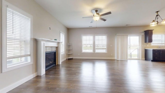 unfurnished living room with a ceiling fan, dark wood-type flooring, a tile fireplace, and a wealth of natural light