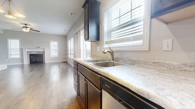 kitchen featuring ceiling fan, a sink, light wood finished floors, light countertops, and a glass covered fireplace