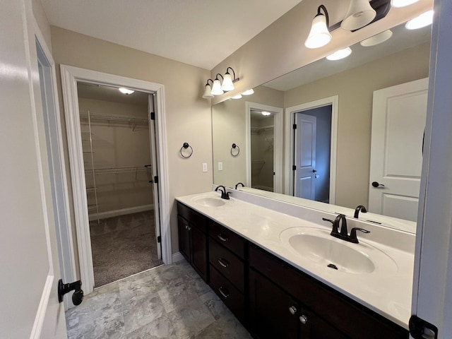 bathroom featuring a sink, baseboards, double vanity, and a spacious closet