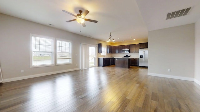 unfurnished living room featuring ceiling fan with notable chandelier, recessed lighting, baseboards, wood finished floors, and visible vents