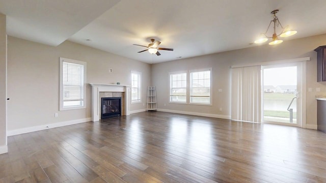 unfurnished living room with a tiled fireplace, a ceiling fan, baseboards, and dark wood-type flooring