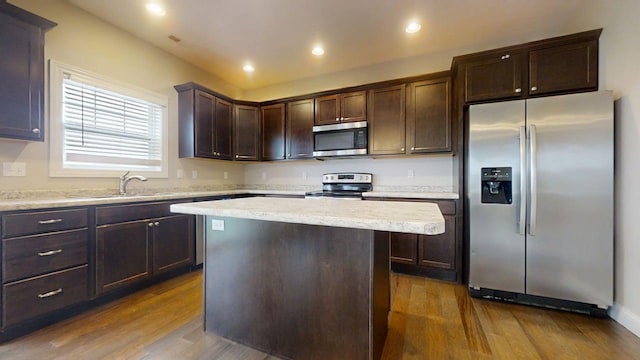 kitchen with dark brown cabinetry, a kitchen island, dark wood-style floors, a sink, and stainless steel appliances