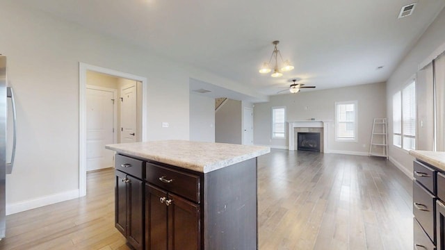 kitchen featuring ceiling fan, light wood finished floors, a fireplace, light countertops, and visible vents