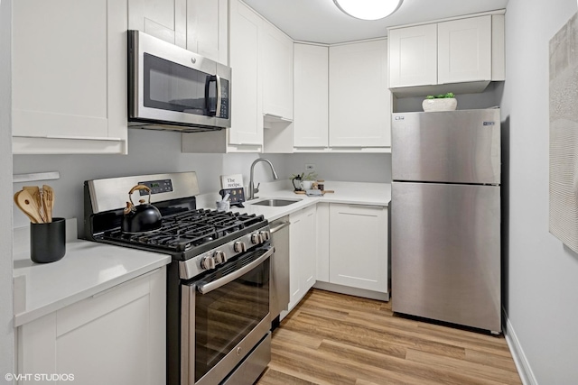 kitchen featuring appliances with stainless steel finishes, a sink, light countertops, white cabinets, and light wood-style floors