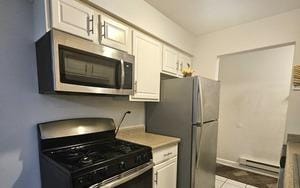 kitchen featuring light tile patterned floors, stainless steel appliances, white cabinetry, a baseboard heating unit, and light countertops