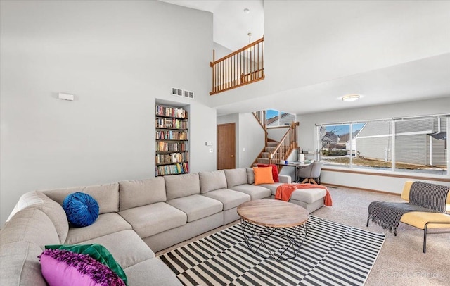 carpeted living room with stairway, a towering ceiling, built in shelves, and visible vents
