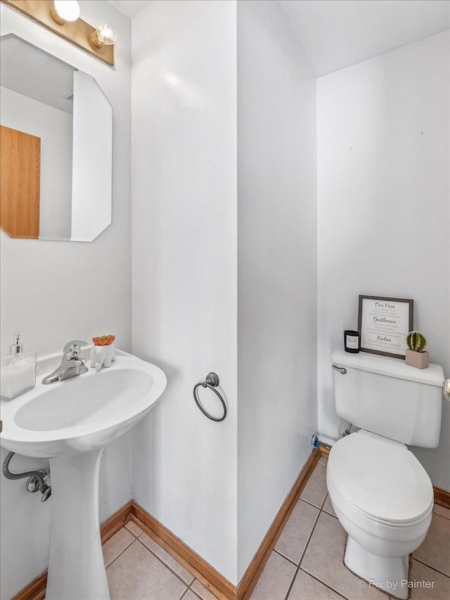 half bath featuring toilet, tile patterned floors, a sink, and baseboards