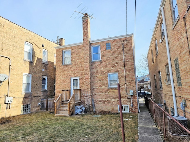 rear view of house featuring central AC, fence, a chimney, brick siding, and a yard