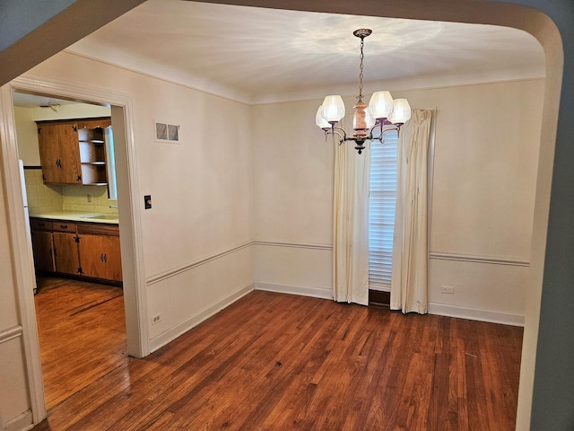 unfurnished dining area featuring an inviting chandelier, a sink, arched walkways, and dark wood-style floors