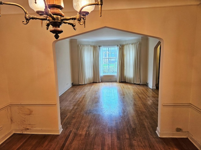 unfurnished dining area with baseboards, arched walkways, wood finished floors, and a chandelier