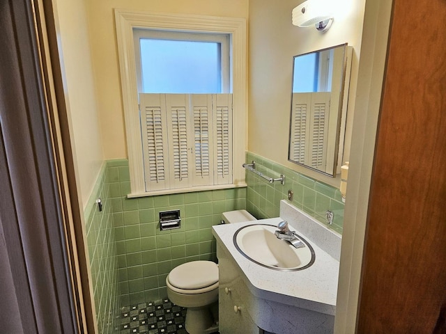 bathroom with vanity, wainscoting, toilet, and tile walls