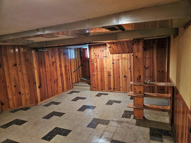 finished basement featuring wooden walls, tile patterned floors, baseboards, and stairway