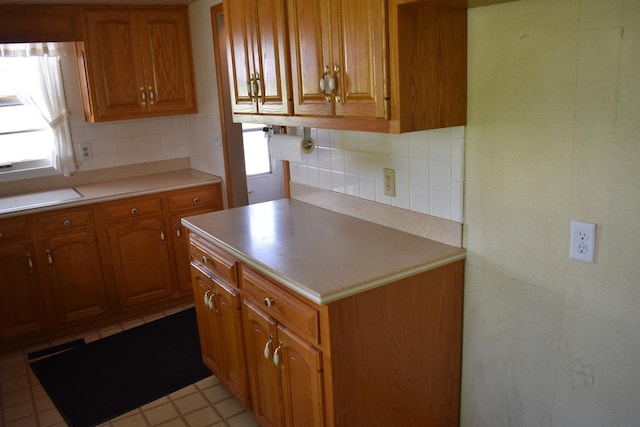 kitchen featuring light countertops, decorative backsplash, brown cabinetry, and a healthy amount of sunlight