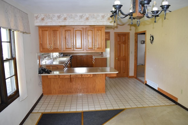 kitchen featuring an inviting chandelier, visible vents, a peninsula, baseboards, and light countertops