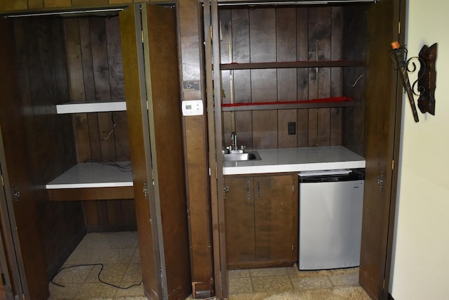 bar featuring a sink, wooden walls, and refrigerator