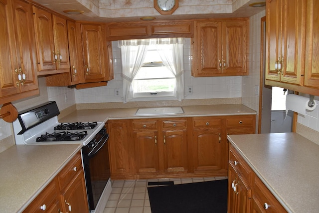 kitchen with range with gas stovetop, decorative backsplash, light tile patterned flooring, light countertops, and brown cabinets