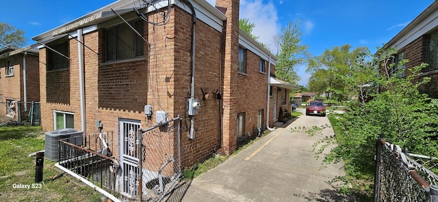 view of side of home with central AC unit, a chimney, and brick siding