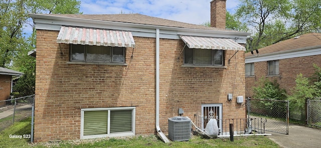 rear view of property with a gate, fence, brick siding, cooling unit, and a chimney
